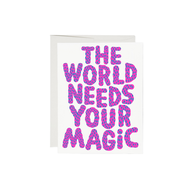 Pink and blue lettering on a white background reading "The World Needs Your Magic". The interior of the card is left blank, while the exterior is 100lb heavyweight card stock, with offset printing. Measuring 5.5 x 4.25 inches, the card features an illustration by Anke Weckmann and is printed in the USA on recycled paper.
